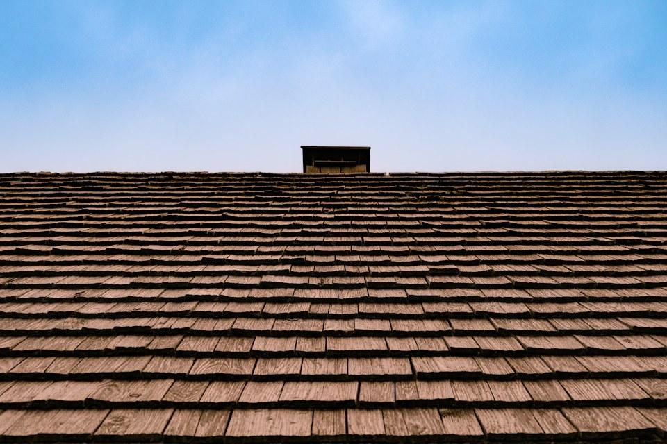 Low view across a shingle roof toward a chimney under a clear sky.